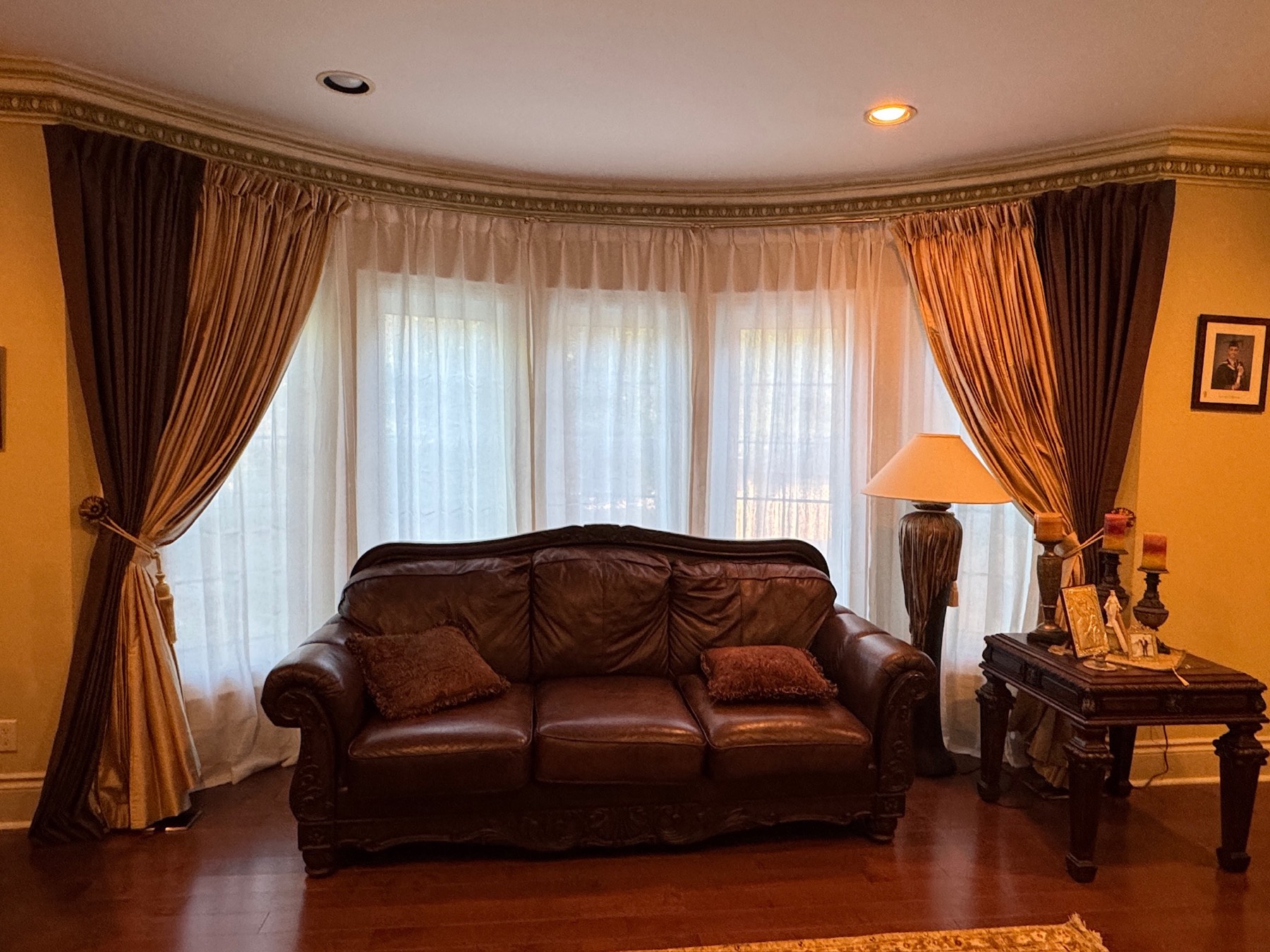 Full-length drapery with sheers and tiebacks across a curved living room bay window, installed by Shadesmen